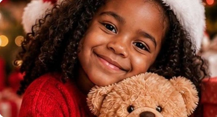Smiling child in a Santa hat hugging a teddy bear beside the Christmas tree